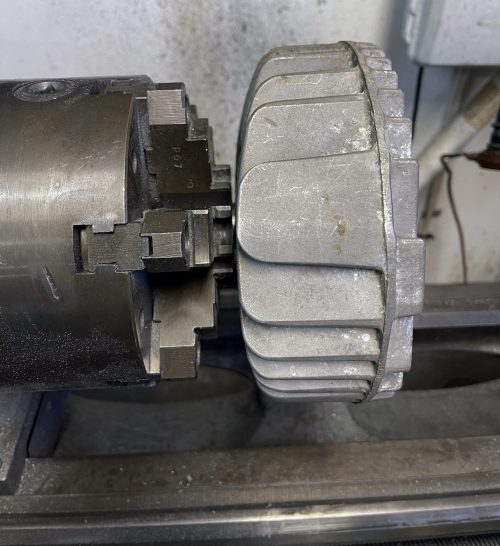 The mandrel should stick out of the lathe chuck or collet just enough to screw on the head and clear the fins. This provides the least amount of runout for accurate machining.